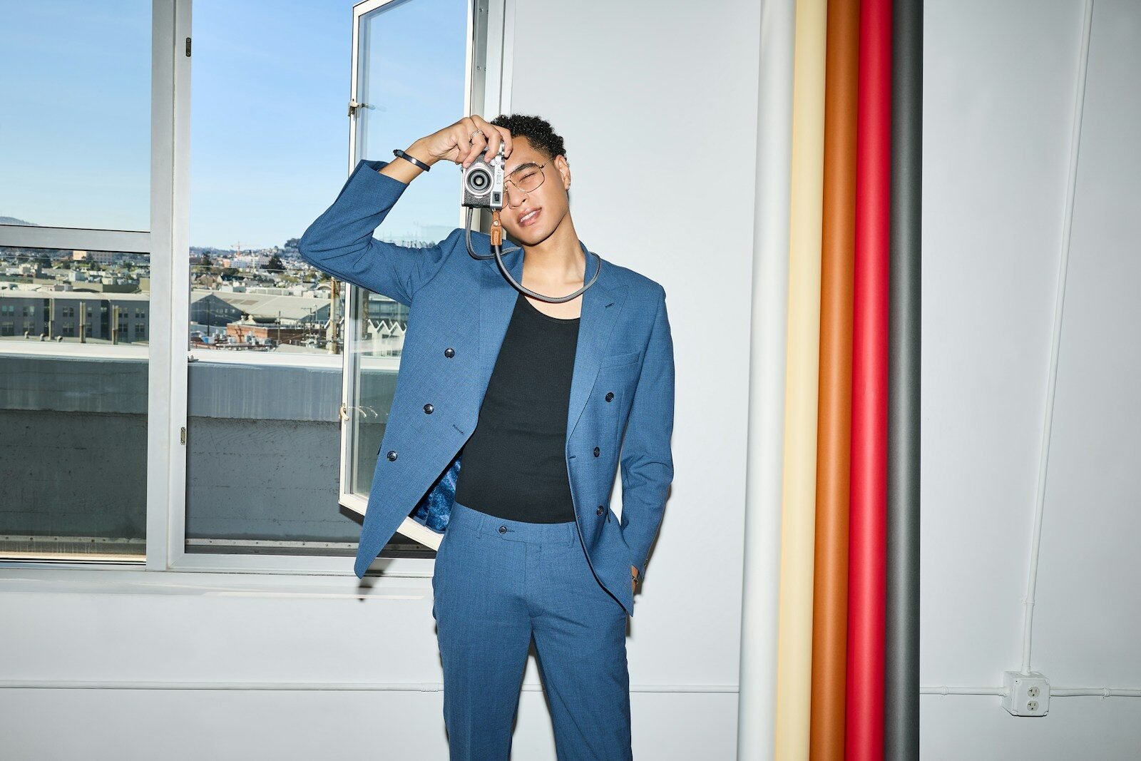 A stylish man in a blue suit holds a camera.