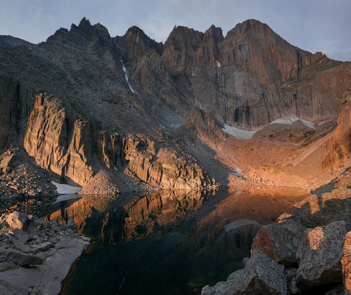 Mountain peaks reflect in a calm lake at sunrise.