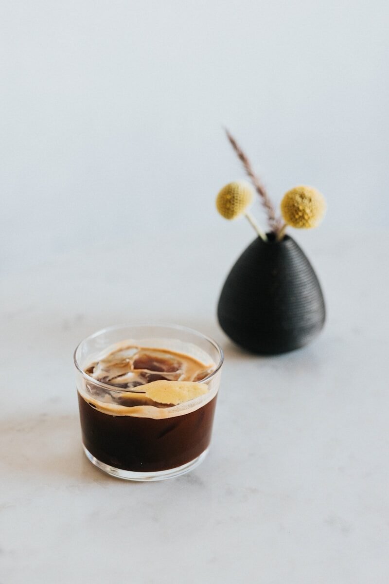 Iced coffee and a black vase with dried yellow flowers.