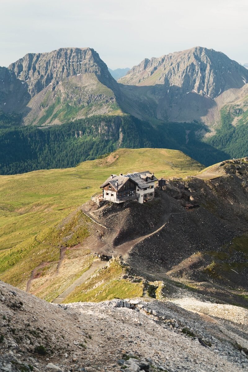 Alpine hut on a rocky mountain ridge with distant peaks.