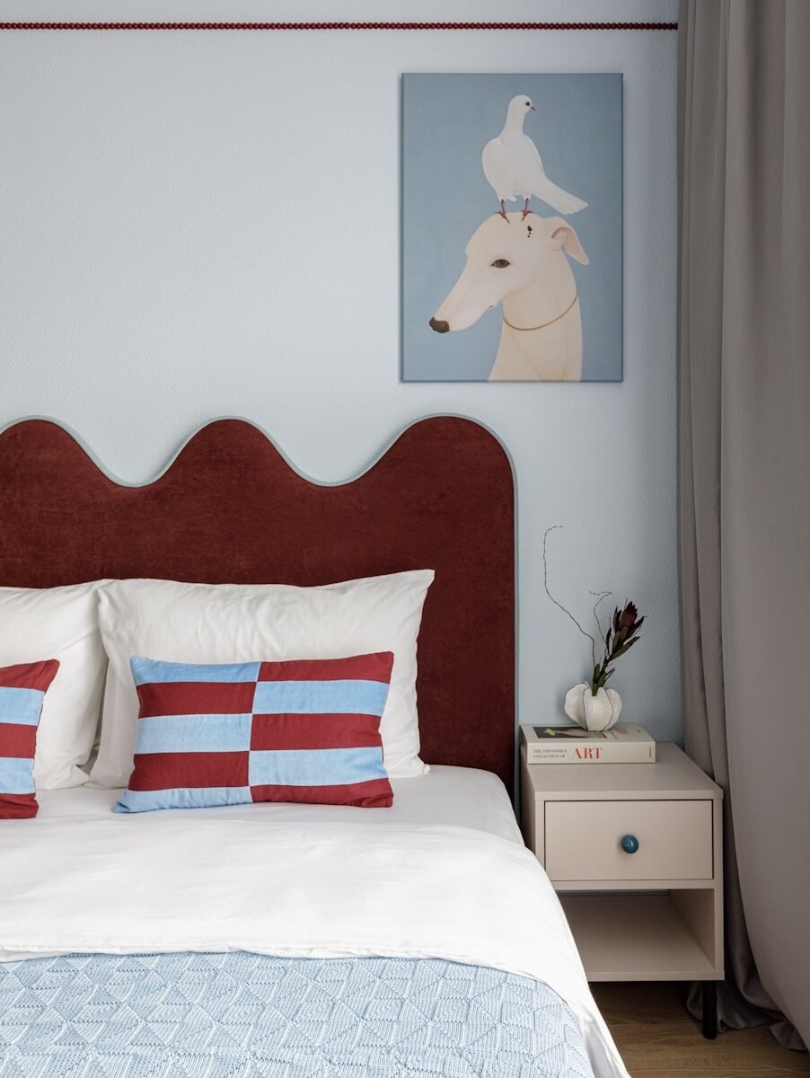 Cozy bedroom with red headboard, striped pillow, and dog painting.